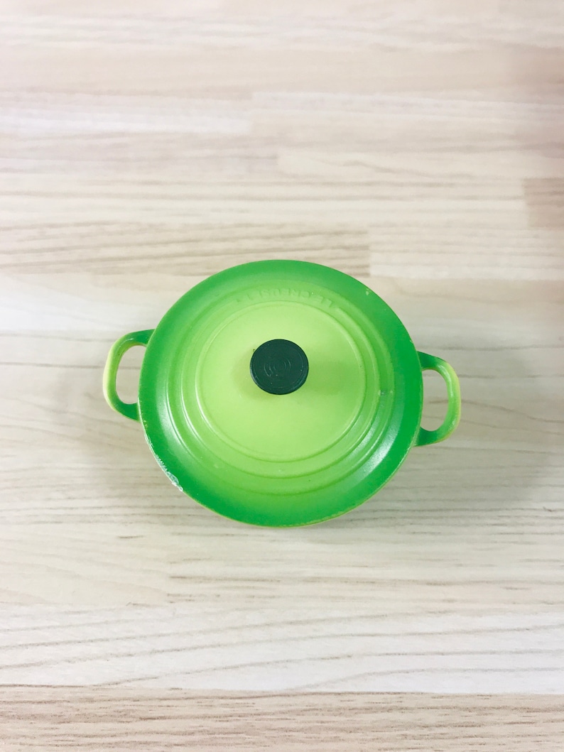 May include: A green enamelled cast iron pot with a black knob on the lid. The pot has two handles.