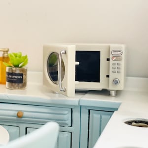 May include: A white microwave with a silver handle and a digital display. The door is open and the microwave is sitting on a light blue countertop.