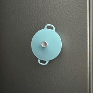 May include: A light blue pot lid with two handles and a silver knob on top.
