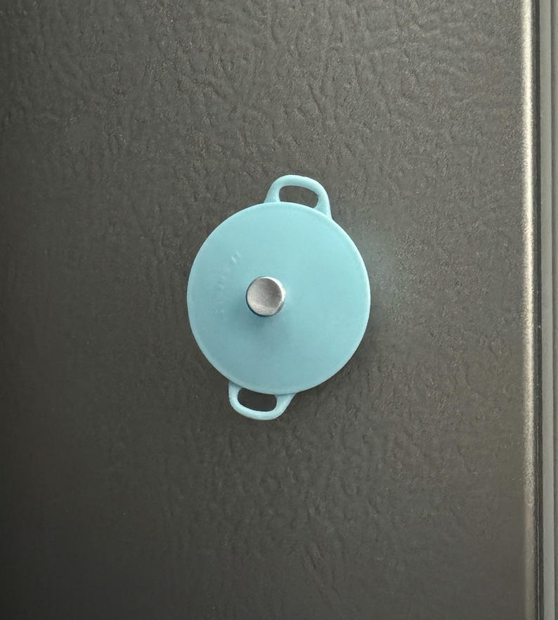 May include: A light blue pot lid with two handles and a silver knob on top.