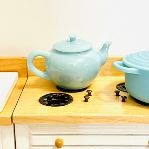May include: A light blue teapot and a light blue pot with a lid on a wooden stovetop with black burner rings and brown knobs.
