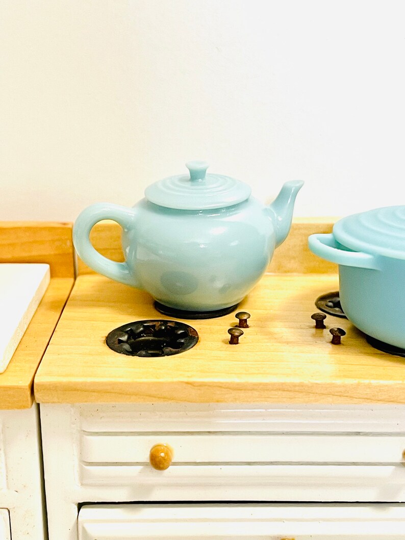 May include: A light blue teapot and a light blue pot with a lid on a wooden stovetop with black burner rings and brown knobs.