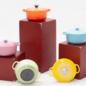 May include: Five miniature cast iron pots in different colours: orange, blue, pink, green and yellow. The pots are arranged on wooden blocks.