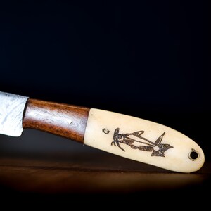 May include: A close-up of a knife with a wooden handle and a bone-like handle with a fish design engraved on it.