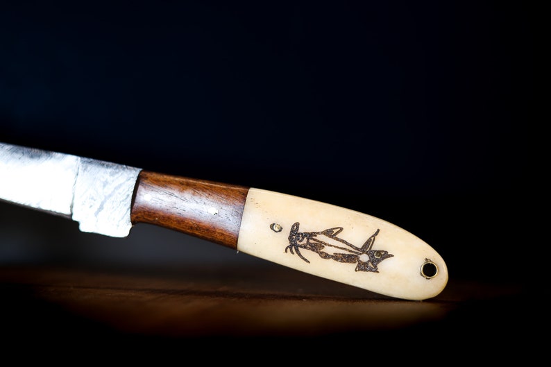 May include: A close-up of a knife with a wooden handle and a bone-like handle with a fish design engraved on it.