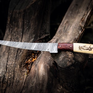 May include: A curved, Damascus steel knife with a wooden and bone handle. The handle has a carved fish design.