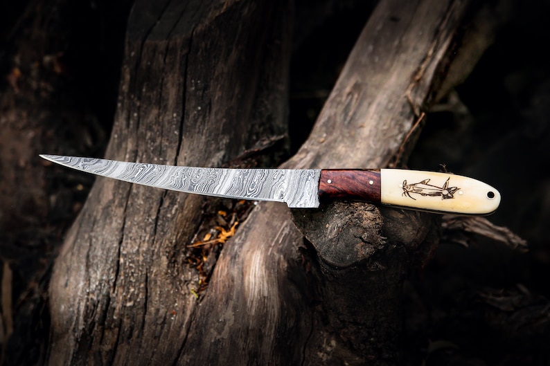 May include: A curved, Damascus steel knife with a wooden and bone handle. The handle has a carved fish design.