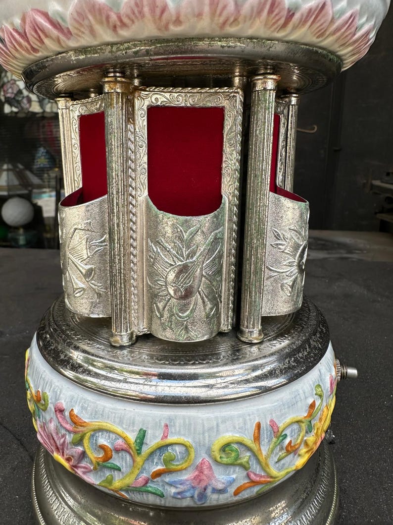 May include: A silver and white porcelain musical carousel with a red velvet interior. The carousel has a floral design and is decorated with silver accents. The carousel is a vintage item and is in good condition.