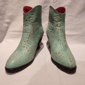 May include: A pair of light green ankle boots with a patterned design. The boots have a pointed toe and a block heel.