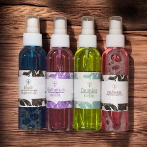 May include: Four small glass bottles with spray tops, each containing a different coloured liquid. The bottles are labelled with the names "Black Chamomile", "Black Amber Vanilla", "Cucumber Melon", and "Cashmere".