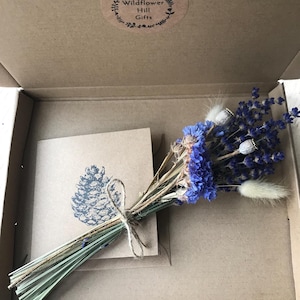 May include: A small bouquet of dried lavender, blue wildflowers, and white bunny tail grass tied with twine. The bouquet is in a brown cardboard box with a card that says "Wildflower Hill Gifts".