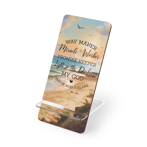 May include: A decorative phone stand featuring a beach scene with a blue sky and ocean. The stand has the words "WAY MAKER, Miracle Worker, PROMISE KEEPER, Light in the Darkness, MY GOD, THAT IS WHO YOU ARE."