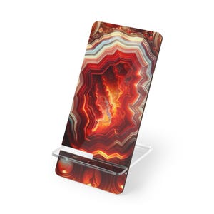 May include: A decorative phone stand featuring a vibrant, abstract design in shades of red, orange, and yellow, resembling a cross-section of an agate stone. The stand has a clear, acrylic base and a slot to hold a phone.