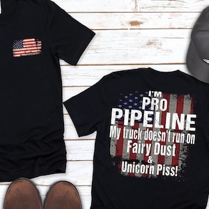 May include: Two black t-shirts with a distressed American flag design. The front of one shirt has a small American flag in the pocket. The back of the other shirt has the text "I'm Pro Pipeline. My truck doesn't run on Fairy Dust & Unicorn Piss!"