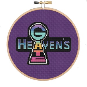Puede incluir: Un aro de bordado morado con un diseño de punto de cruz de una llave arcoíris con el texto "GAY HEAVEN'S" en fuente pixelada.