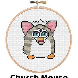 Puede incluir: Bordado de punto de cruz de una criatura parecida a un Furby en un aro de madera. La criatura tiene pelaje a rayas grises y blancas, orejas rosas, ojos azules y un pico naranja. El texto "Church Mouse" está debajo.