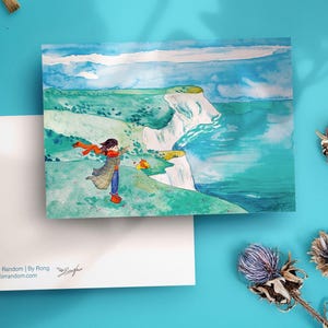 May include: A watercolour print of a coastal scene with a person in a red scarf. The artwork is on a white card, with paintbrushes and dried flowers on a blue surface. The card has text that reads "@Fall for Random | By Rong" and "www.fallforrandom.com".