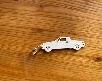 May include: White metal keychain shaped like a vintage car. The keychain has a silver ring for attaching to keys.