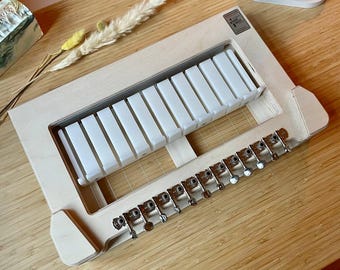 May include: A wooden soap mold with a grid pattern and 10 individual compartments. The mold has a row of metal knobs along the bottom edge. The mold is made of light wood and has a natural finish.