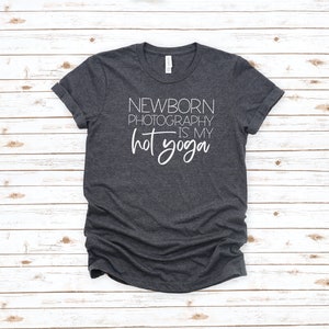 Peut inclure: Un t-shirt gris fonc&eacute; avec le texte "NEWBORN PHOTOGRAPHY IS MY HOT YOGA" imprim&eacute; en blanc.