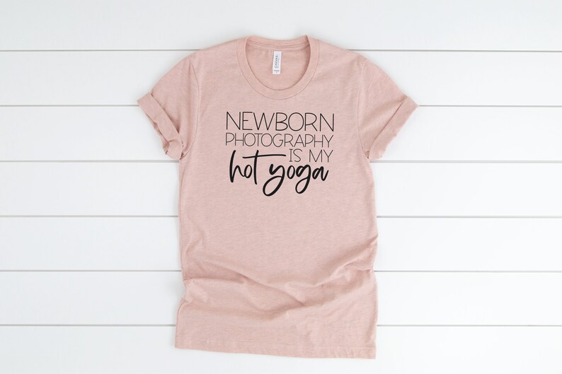 Peut inclure: Un t-shirt rose p&acirc;le avec le texte "NEWBORN PHOTOGRAPHY IS MY HOT YOGA" imprim&eacute; en noir.