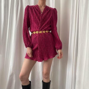 May include: A pink and white patterned dress with long sleeves and a wrap-style bodice. The dress has a gold chain belt with circular links.