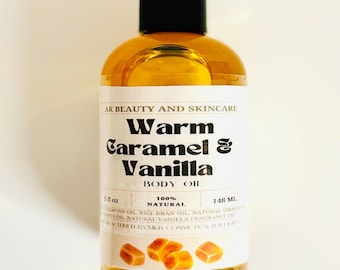 May include: A clear glass bottle with a black cap filled with a golden liquid. The bottle label reads "AK Beauty and Skincare Warm Caramel & Vanilla Body Oil 100% Natural 5 oz 148 ml". The label also features a drawing of caramel candies.