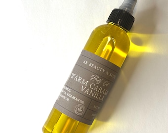 May include: A clear plastic squeeze bottle filled with golden yellow body oil. The label reads AK BEAUTY & SKIN, Body Oil, WARM CARAMEL VANILLA, and lists ingredients including rice bran oil and fragrance oil. It has a black cap and a clear nozzle.
