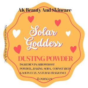 May include: An orange label with the text "AK Beauty And Skincare" at the top. The label reads "Solar Goddess DUSTING POWDER" with ingredients listed below. The label is decorated with red and white hearts. The product contains 113 grams.