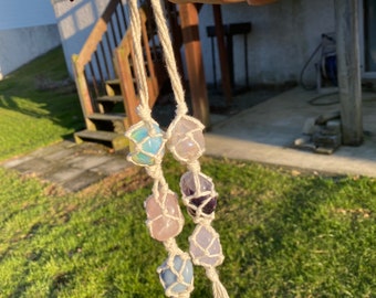 May include: A macrame crystal necklace with five crystals in a variety of colors, including pink, purple, blue, and green. The necklace is made with white string and has a tassel at the end.
