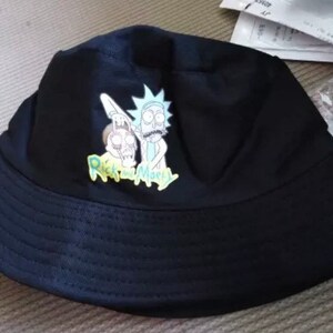 May include: Black bucket hat with a graphic print of Rick and Morty characters. The text "Rick and Morty" is printed in yellow on the hat.