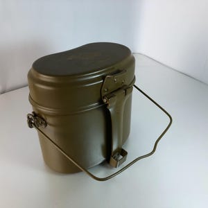 May include: A green metal camping mess kit with a handle. The kit has two nesting pots and a lid.
