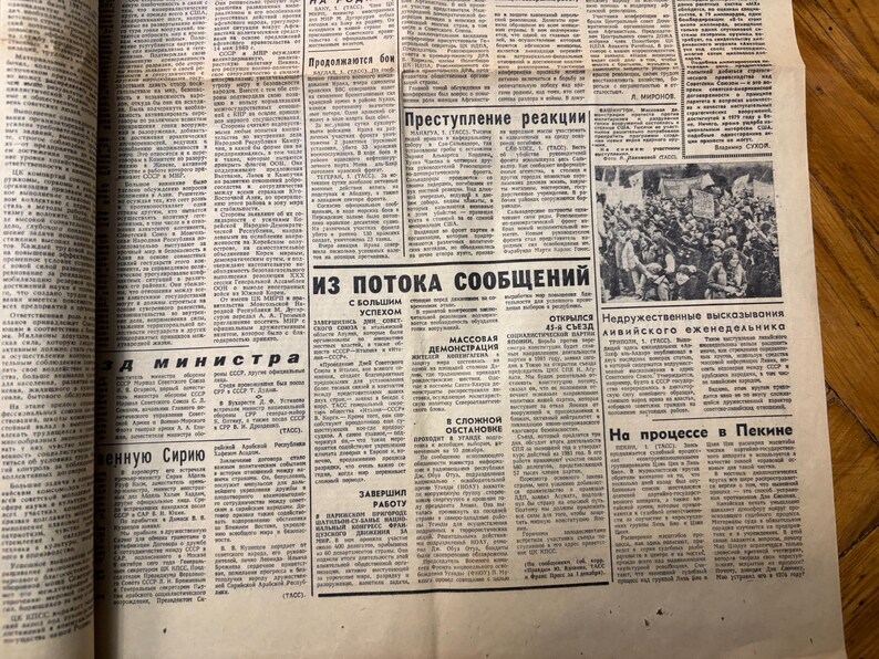 May include: A black and white newspaper page with the headline "Из потока сообщений" (From the flow of messages) and a photo of a crowd of people. The text on the page is in Russian.