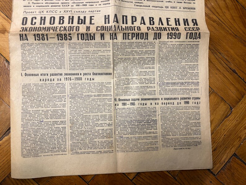 May include: A black and white newspaper headline reads "Основные направления экономического и социального развития СССР на 1981-1985 годы и на период до 1990 года" which translates to "Basic Directions of Economic and Social Development of the USSR for 1981-1985 and for the period until 1990".