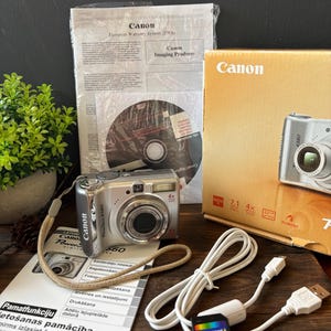 以下が含まれることがあります： リストストラップ付きのシルバーのキヤノンPowerShot A560デジタルカメラ、タンカラーの製品箱、Transcend製128MBメモリーカード、白いUSBケーブル、ソフトウェアディスク、およびキヤノンのロゴと製品仕様が記載された印刷済みの取扱説明書。
