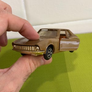 以下が含まれることがあります： ドアが開いた茶色の玩具の車。車は黒い車輪と詳細なフロントグリルを持っています。
