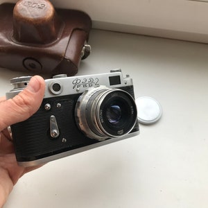 Może przedstawiać: Srebrny i czarny aparat fotograficzny 35 mm z obiektywem oznaczonym "Industar 50-2". Aparat ma czarny sk&oacute;rzany futerał.
