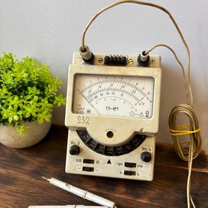 May include: Vintage beige analog multimeter with a dial face, multiple settings, and attached probes. The meter has the text "ТЛ-4М" and "232" printed on it. The device is on a wooden surface.