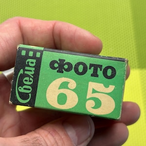 Puede incluir: Una caja de película verde y negra con el texto "Фото 65" y "Свеча" impreso en ella.