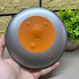 May include: A silver and orange portable sport audio player by Philips with the Nike logo. The player has an orange center with directional buttons and the text "Portable Sport Audio by Philips".