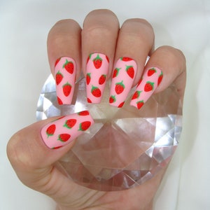 May include: Pink long false nails with a strawberry print design.