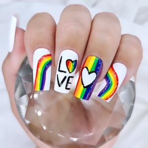 May include: Close-up of a hand with rainbow-painted nails. Each nail features a different design, including a rainbow, a heart, and the word "LOVE".