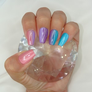 May include: A hand model wearing a set of five long, coffin-shaped artificial nails with a gradient of pink, purple, and blue nail polish.