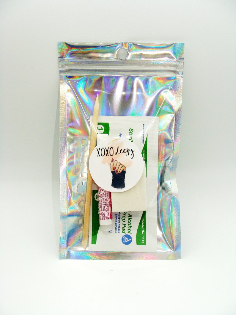 May include: A silver iridescent zippered pouch containing a small bottle of alcohol prep pads, two wooden cuticle sticks, and a white sticker with the text "XOXO Leesy" and a graphic of a hand with red nail polish.