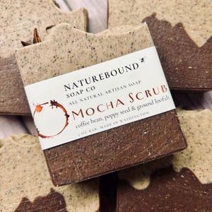 May include: A brown and beige bar of soap with a white label that reads "NATUREBOUND SOAP CO ALL NATURAL ARTISAN SOAP MOCHA SCRUB coffee bean, poppy seed & ground loofah 5 OZ BAR. MADE IN WASHINGTON"