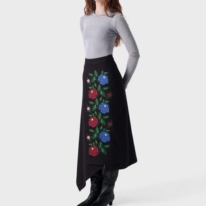 May include: Black skirt featuring a floral embroidery design in red and blue. The skirt has an asymmetrical cut and is worn with a grey long-sleeved top and black boots. The floral pattern is a key detail.