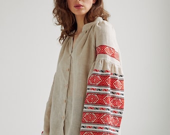 May include: A beige linen shirt with red and black embroidered details on the sleeves. The shirt has a v-neck and button closure.