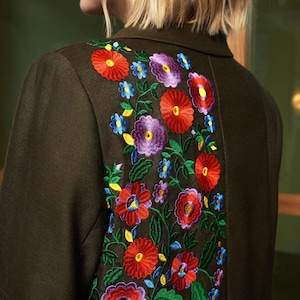 Pode incluir: Um blazer verde escuro com um design de bordado floral colorido nas costas. O bordado apresenta flores vermelhas, amarelas, azuis, roxas e verdes.