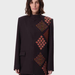 May include: A dark brown blazer with a high collar and long sleeves. The blazer features an embroidered floral design in red, orange, and green on the front and shoulder. The blazer has a single pocket.
