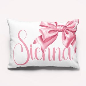 May include: A white pillow with a pink bow and the name "Sienna" written in pink cursive.